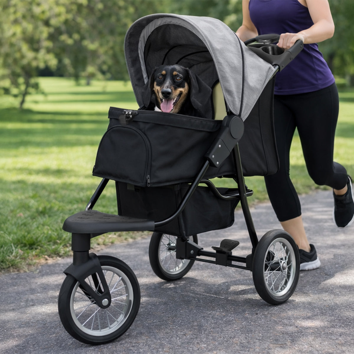 Grå husdjursvagn med svart tyg, stora hjul och en bekväm korg för hundar, perfekt för promenader i parken