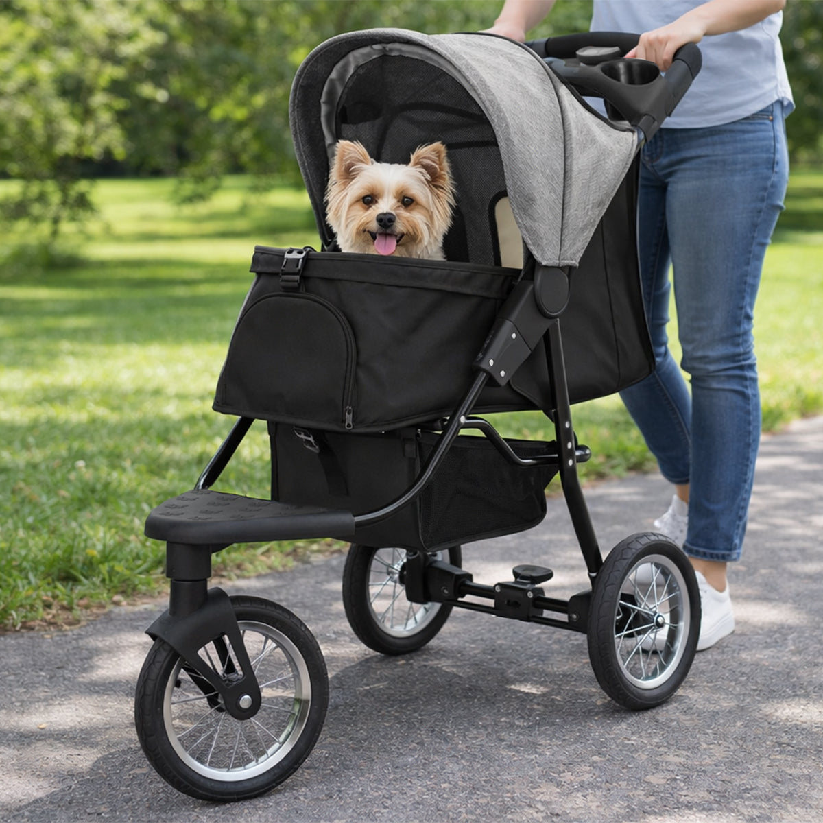 Grå husdjursvagn med en glad hund inuti, stora hjul och en mjuk, vadderad sittdel, perfekt för promenader i parken