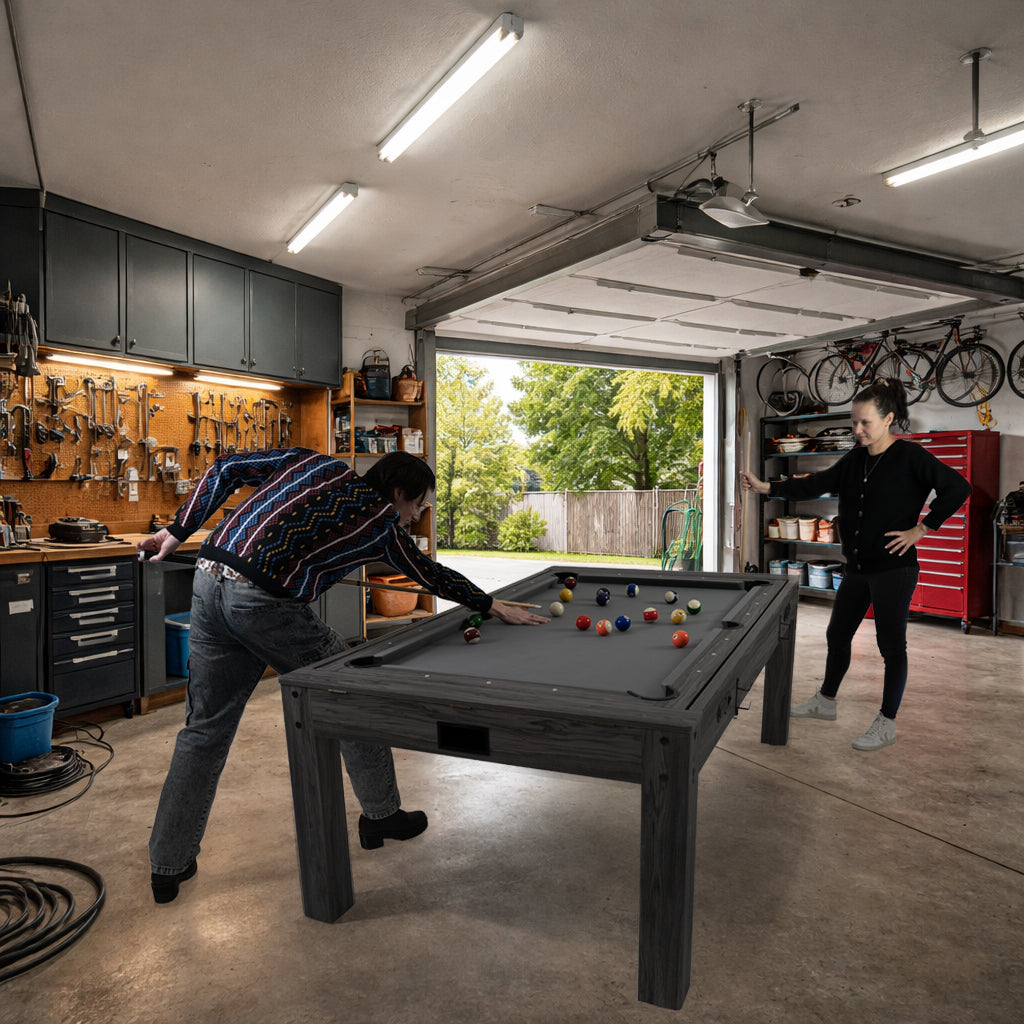 Grått 7-i-1 spelbord med dartpaket och LED-lampa, två personer spelar biljard i en garageinredning med verktyg och cyklar