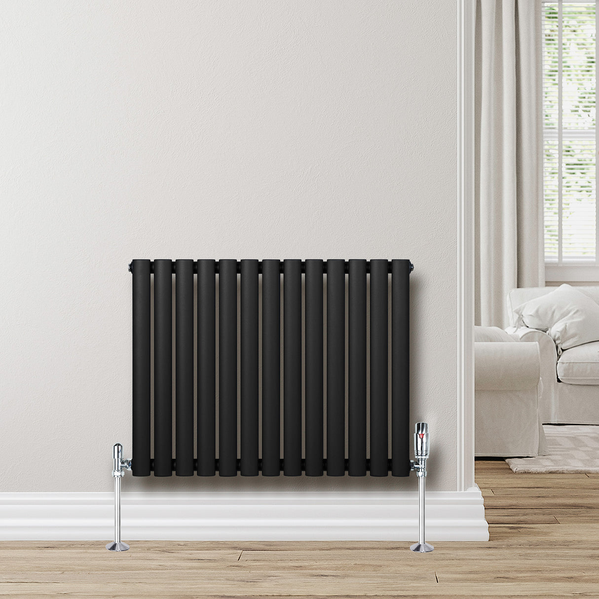 Oval svart enkelkolonnsradiator med glänsande ventiler, placerad mot en ljus vägg i ett modernt rum med trälookgolv
