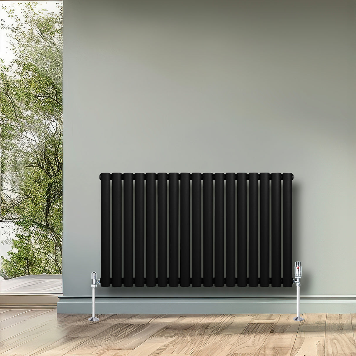 Oval svart enkelkolonnsradiator med släta ytor och vertikala ribbor, placerad mot en ljus vägg i ett rum med trägolv