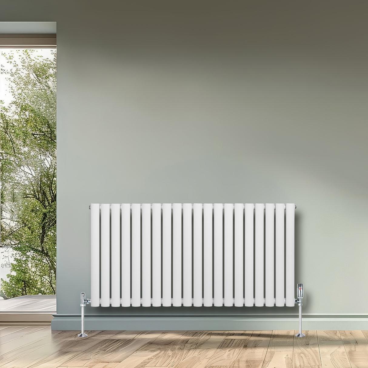 Oval vit enkelpelarradiator med släta, vertikala ribbor, placerad mot en grön vägg och ett fönster med utsikt mot trädgården