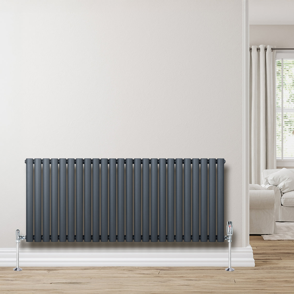 Oval enkelkolonnsradiator i antracitgrå med släta, vertikala ribbor och kromade ventiler, placerad mot en ljus vägg