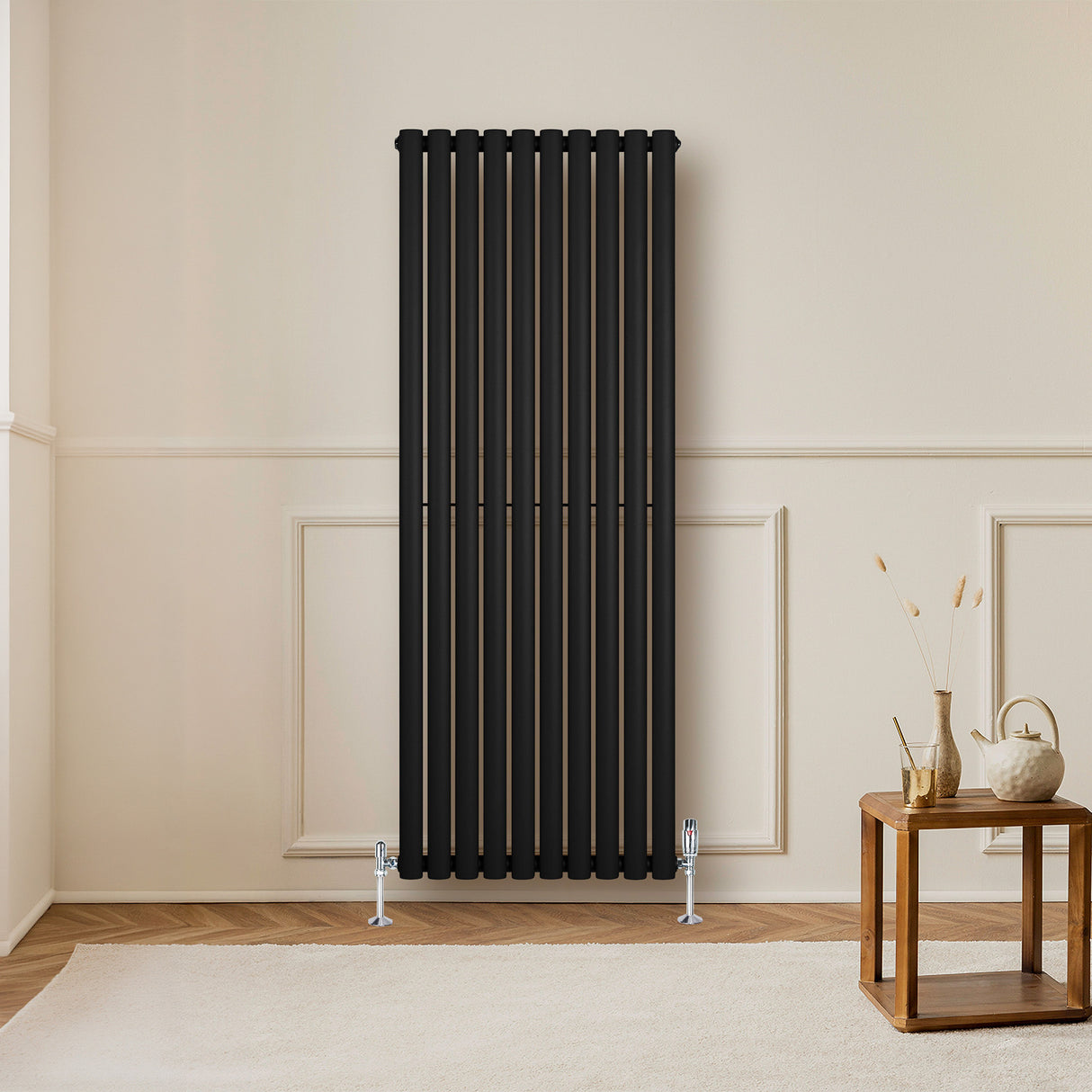 Oval svart enkelkolonnsradiator med släta ytor och vertikala ribbor, placerad på en ljus vägg i ett stilrent rum med möbler