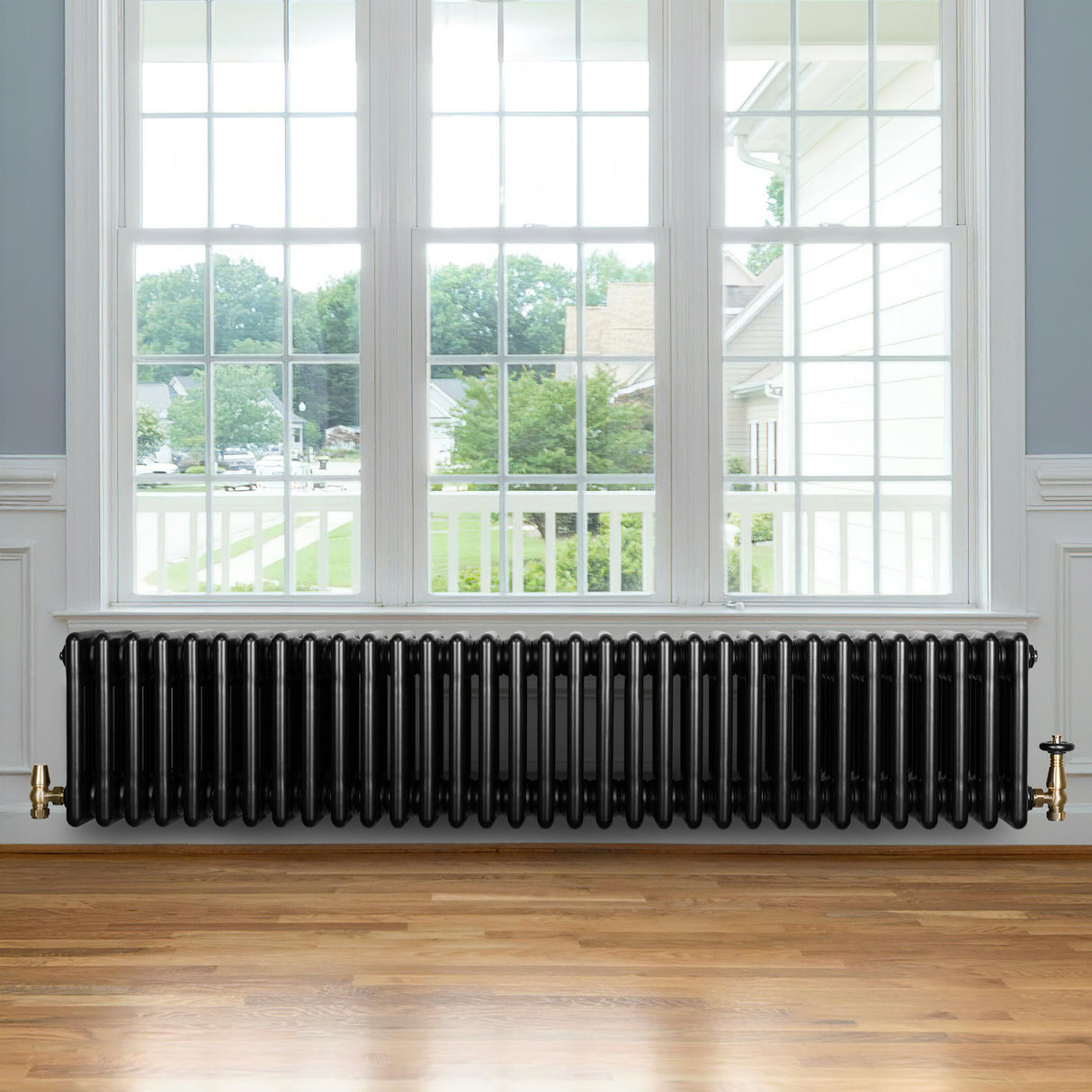 Svart traditionell 4-kolonnsradiator med glänsande yta, placerad under fönster med trädetaljer och ljus parkettgolv