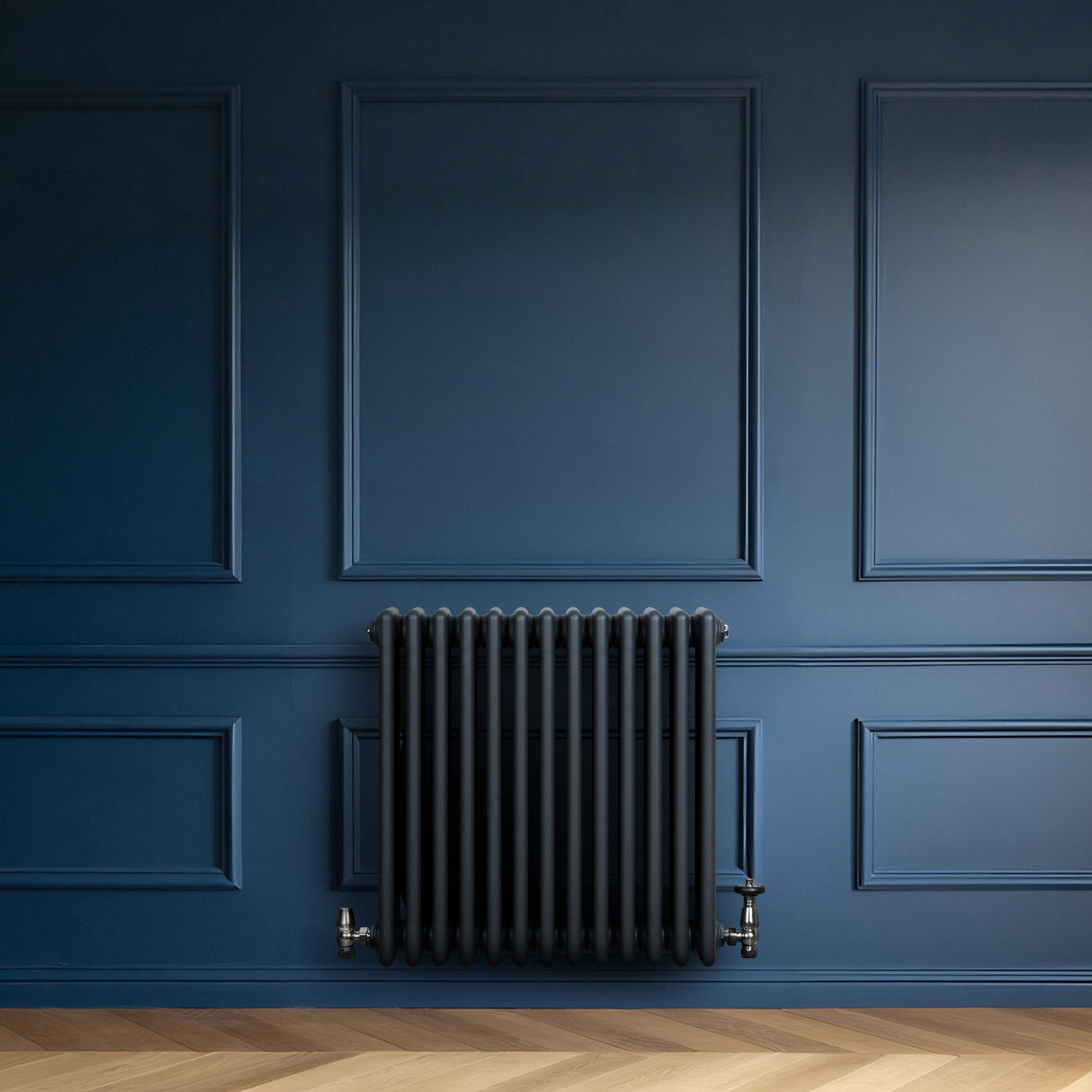 Traditionell antracitgrå 4-kolonnsradiator med släta ytor, placerad mot en mörkblå vägg i ett elegant rum med träparkett