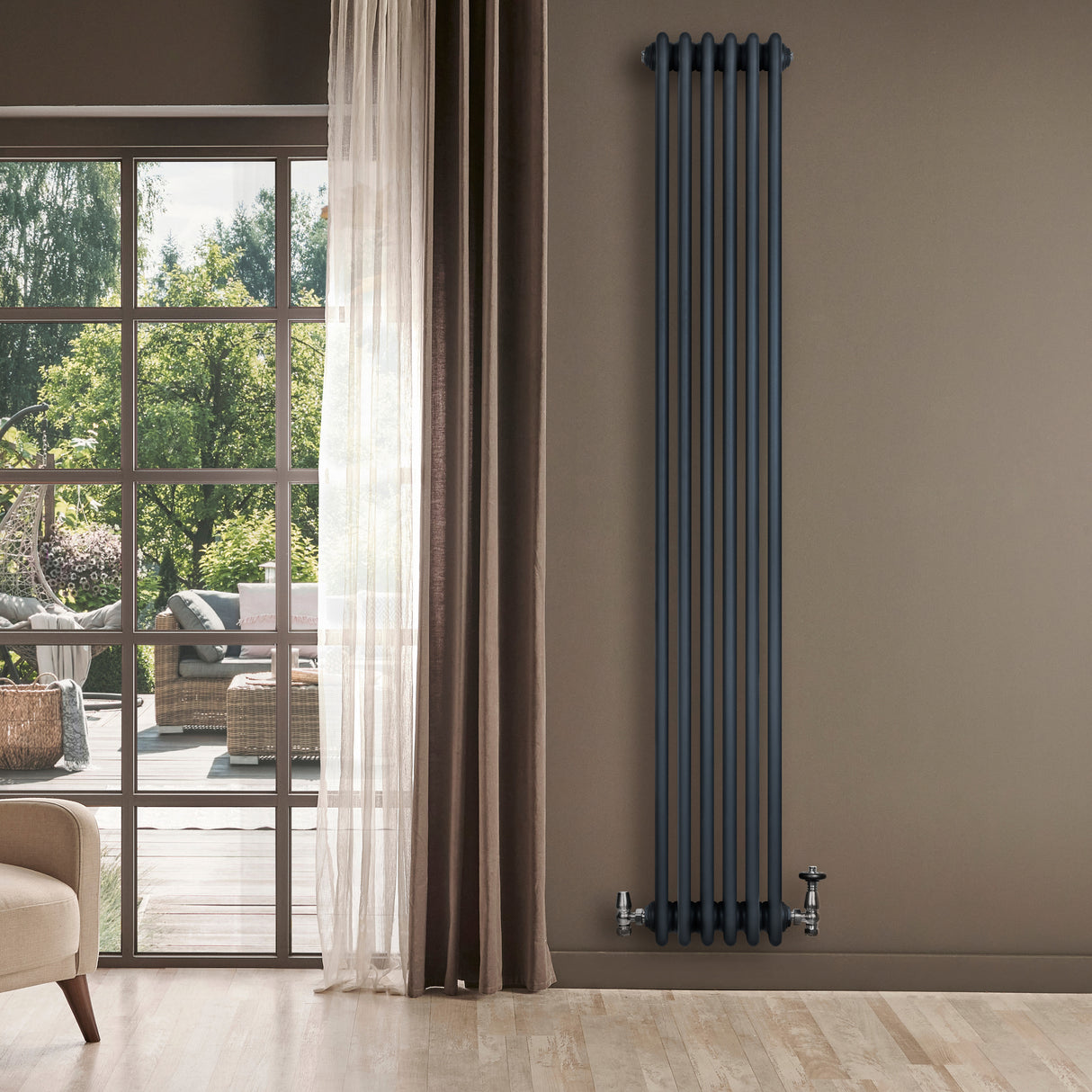 Traditionell antracitgrå 4-kolonnsradiator med släta ytor, installerad på en vägg nära stora fönster och en bekväm fåtölj