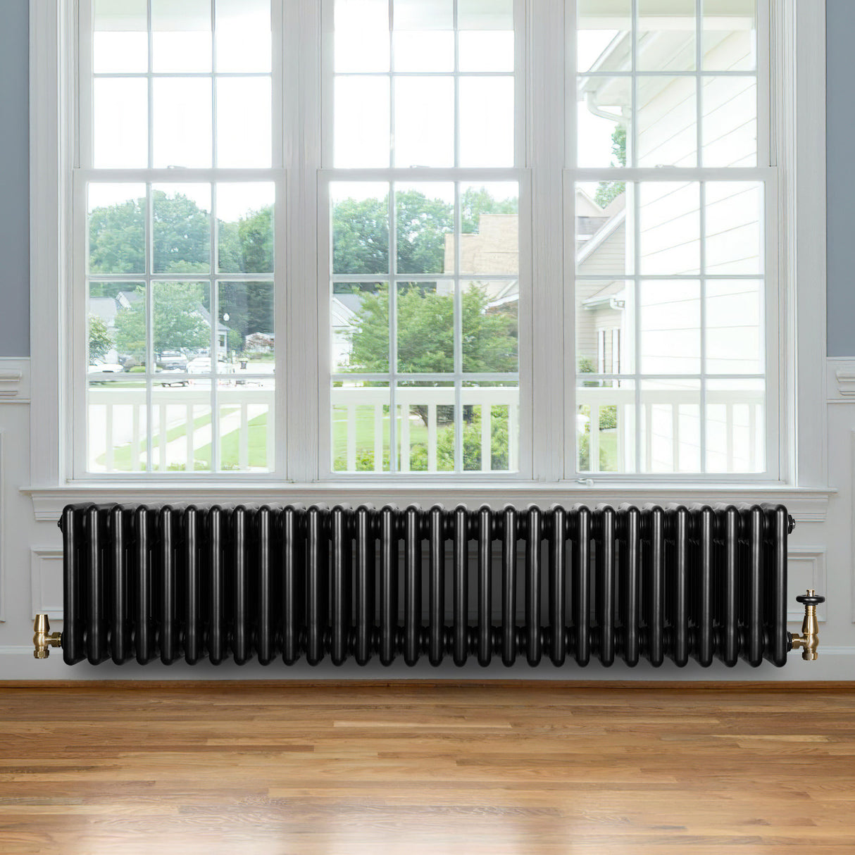 Svart traditionell 4-kolonnsradiator i metall, 300 x 1370 mm, placerad under ett stort fönster med trädetaljer och parkettgolv