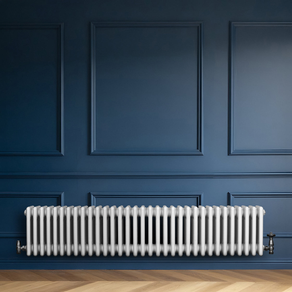 Traditionell vit 4-kolonnsradiator i metall, placerad längs en blå vägg, med släta, rundade former och synliga röranslutningar