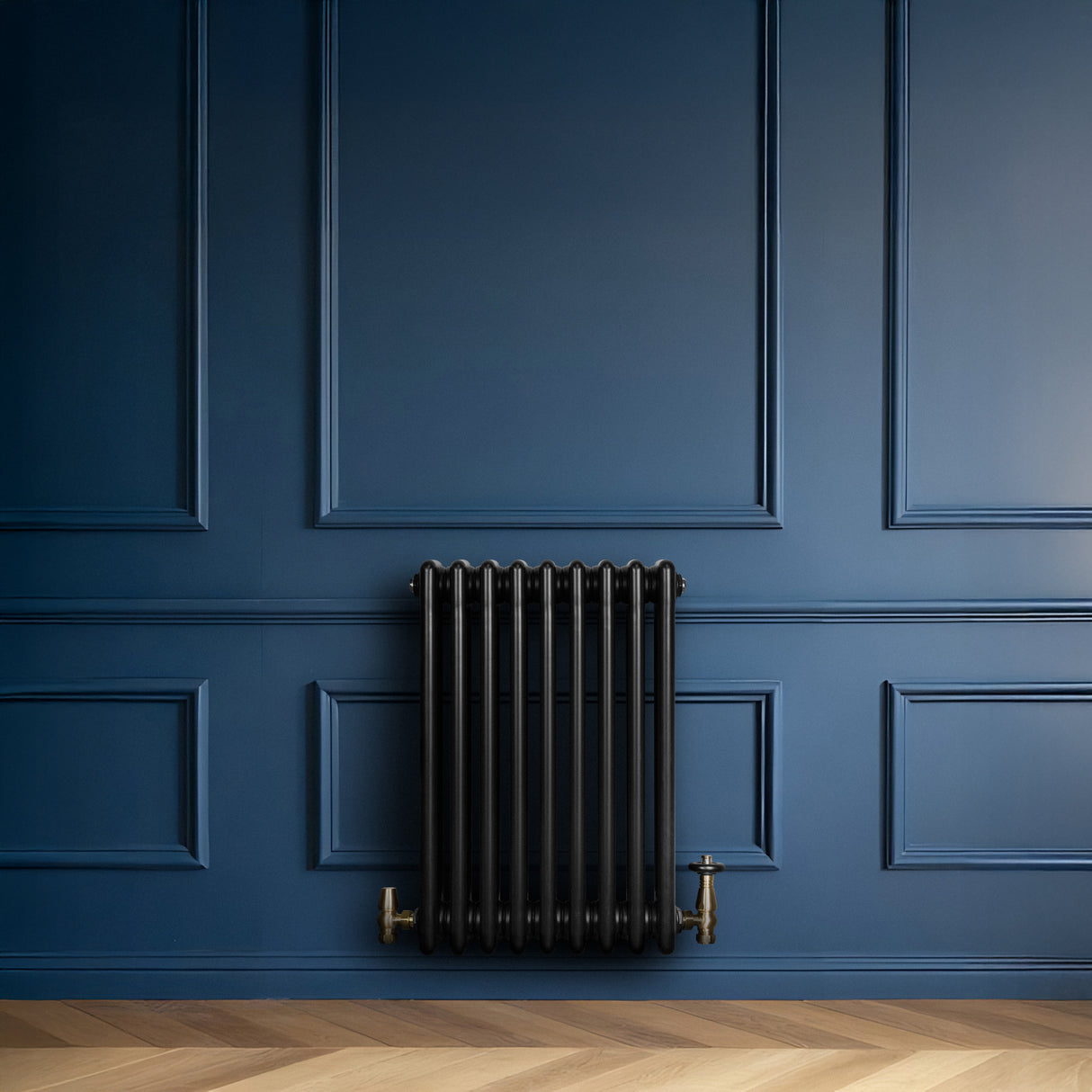 Svart traditionell 4-kolonnsradiator i metall, placerad mot en mörkblå vägg med eleganta paneler och ett ljust trägolv