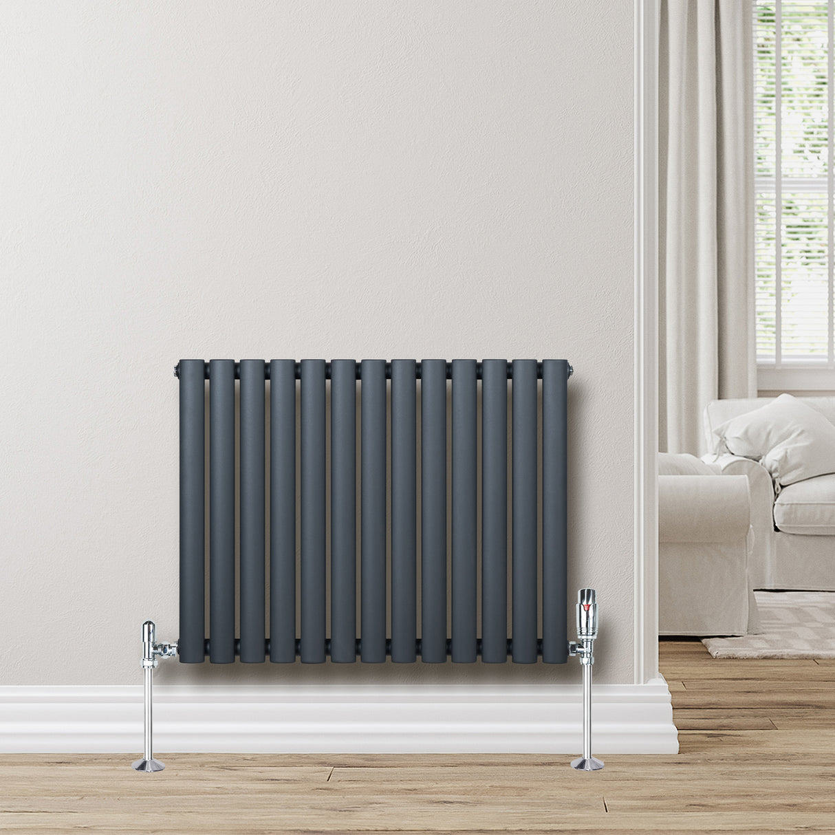 Oval enkelpelarradiator i antracitgrå, med släta ytor och vertikala rör, installerad på en ljus vägg i ett modernt rum
