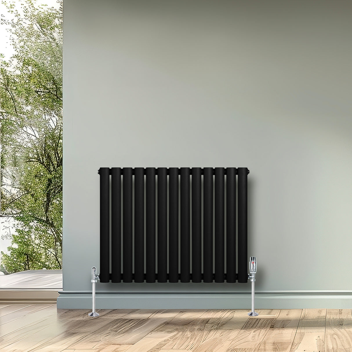 Oval svart enkelpelarradiator med släta, vertikala ribbor, monterad på en ljus vägg i ett rum med utsikt mot grönska