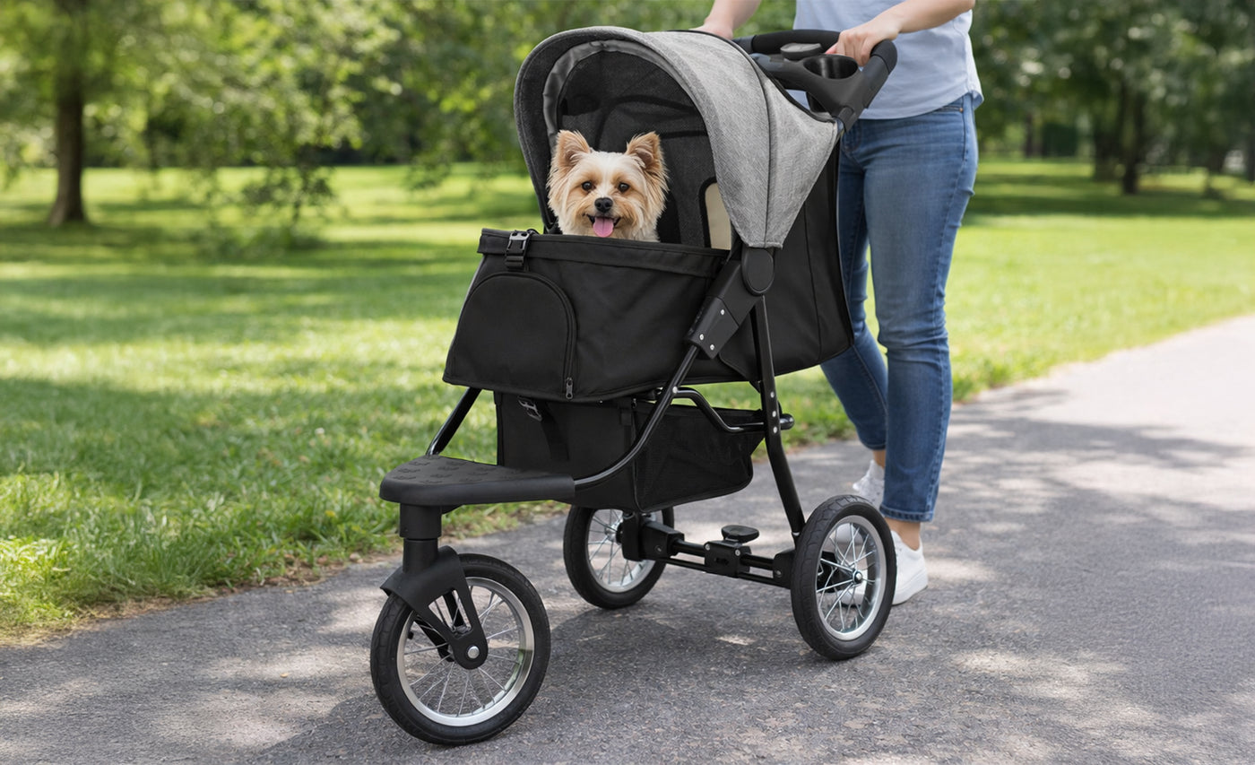 Hundvagn i svart och grått med en glad hund inuti, som körs av en person på en grön parkstig omgiven av träd