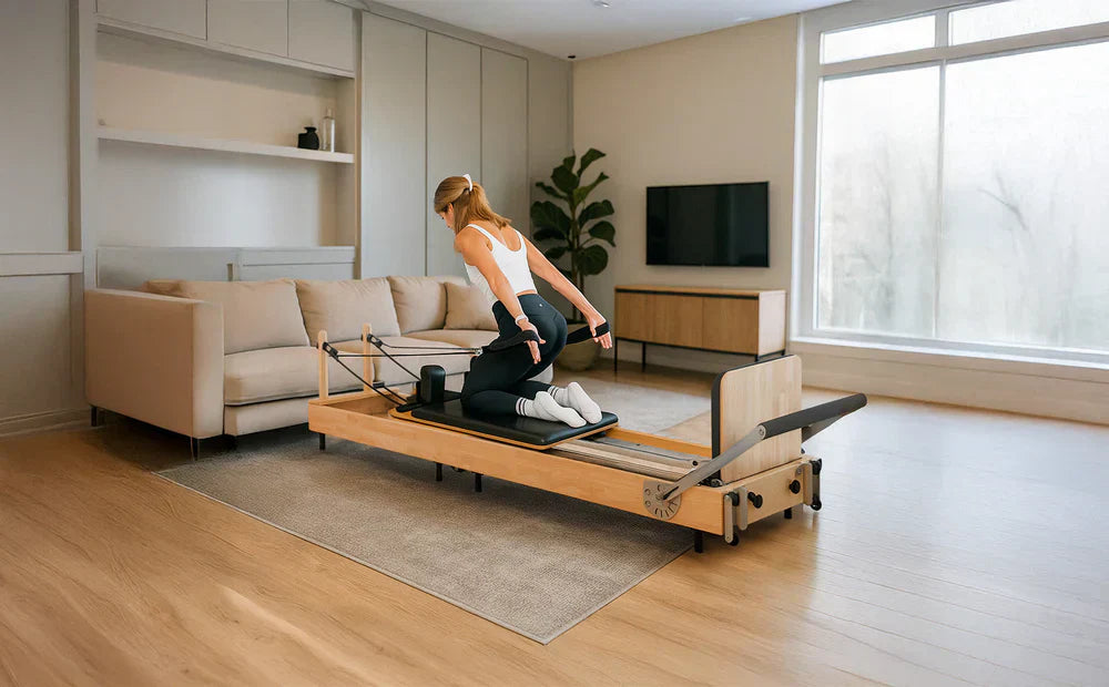 Kvinna i sportkläder utför Reformer Pilates på en träbänk i ett ljust rum med en soffa och stor fönster för naturligt ljus