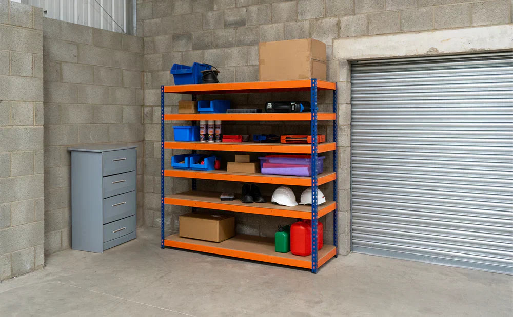 Ett robust hyllsystem med orange hyllor och blå lådor, placerat i ett garage med grå väggar och en rullport i bakgrunden
