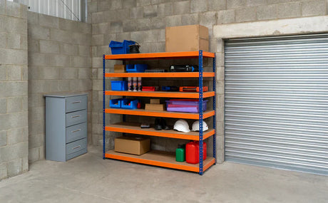 Ett robust hyllsystem med orange hyllor och blå lådor, placerat i ett garage med grå väggar och en rullport i bakgrunden