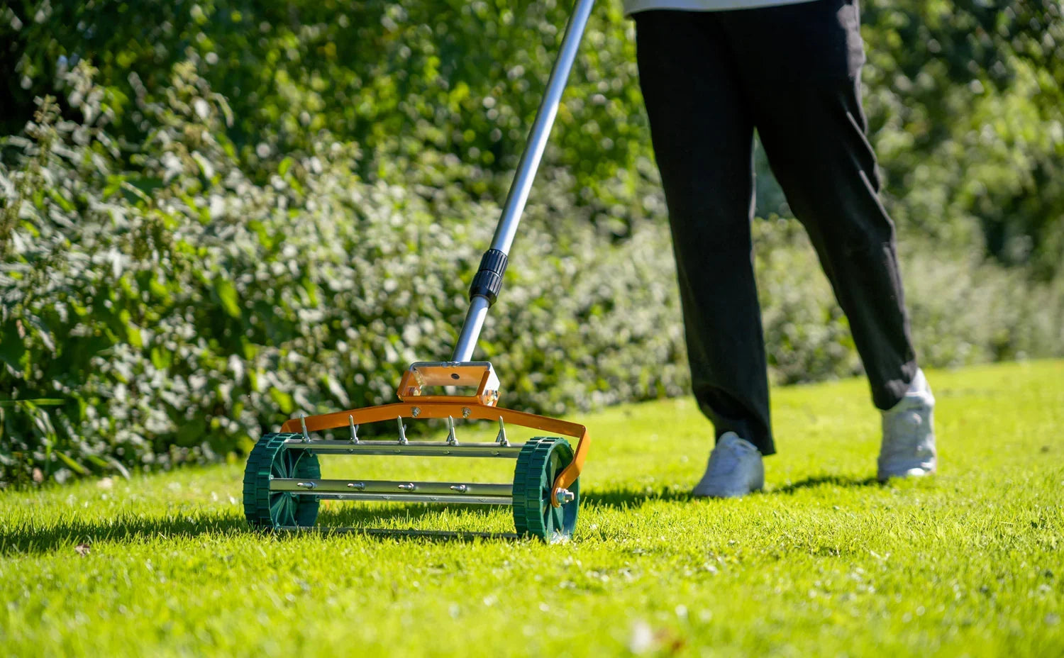 En person använder en gräsklippare med orange och grön design på en grön gräsmatta, omgiven av frodig vegetation