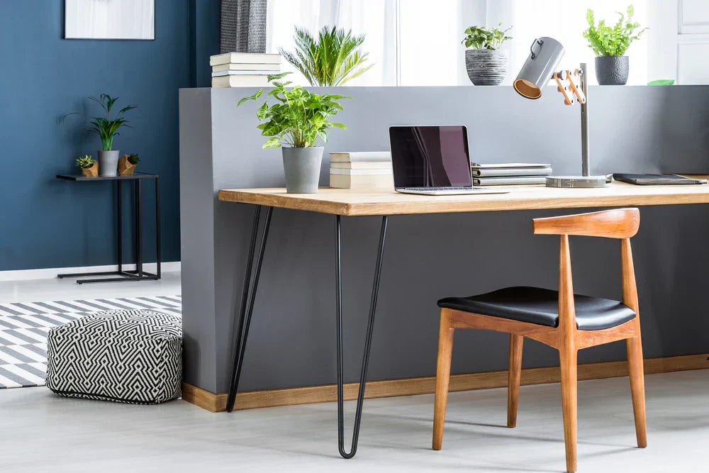 Ett stilrent arbetsrum med en träbord, svart stol, laptop, växter och en modern lampa mot en blå vägg