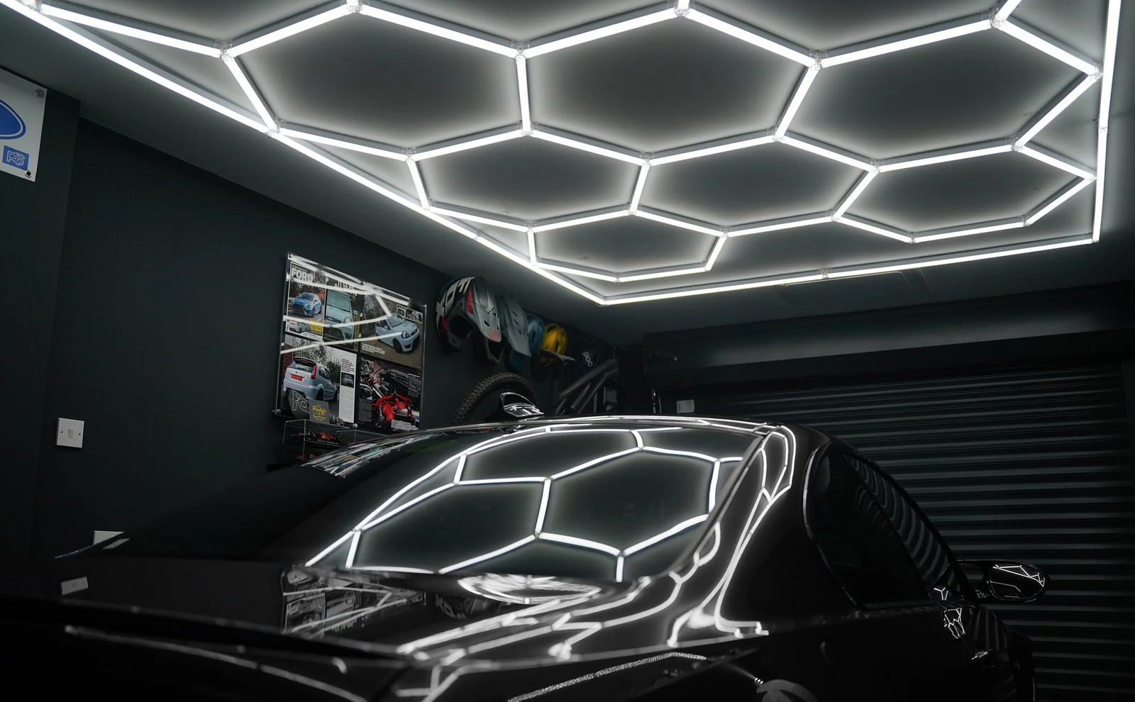 Hexagonformad LED-belysning i taket av ett garage, reflekterande på en svart bil, skapar en modern och stilren atmosfär