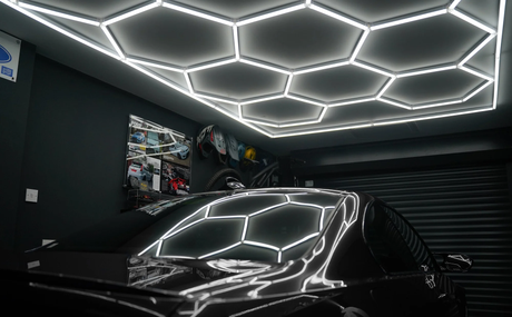 Hexagonformad LED-belysning i taket av ett garage, reflekterande på en svart bil, skapar en modern och stilren atmosfär