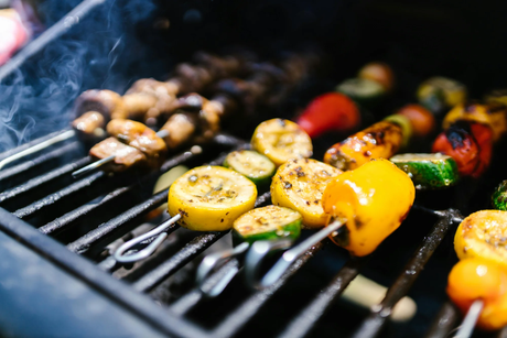Färgglada grönsaksspett med paprika, zucchini och svamp grillas på en kolgrill, omgiven av rök och glödande kol