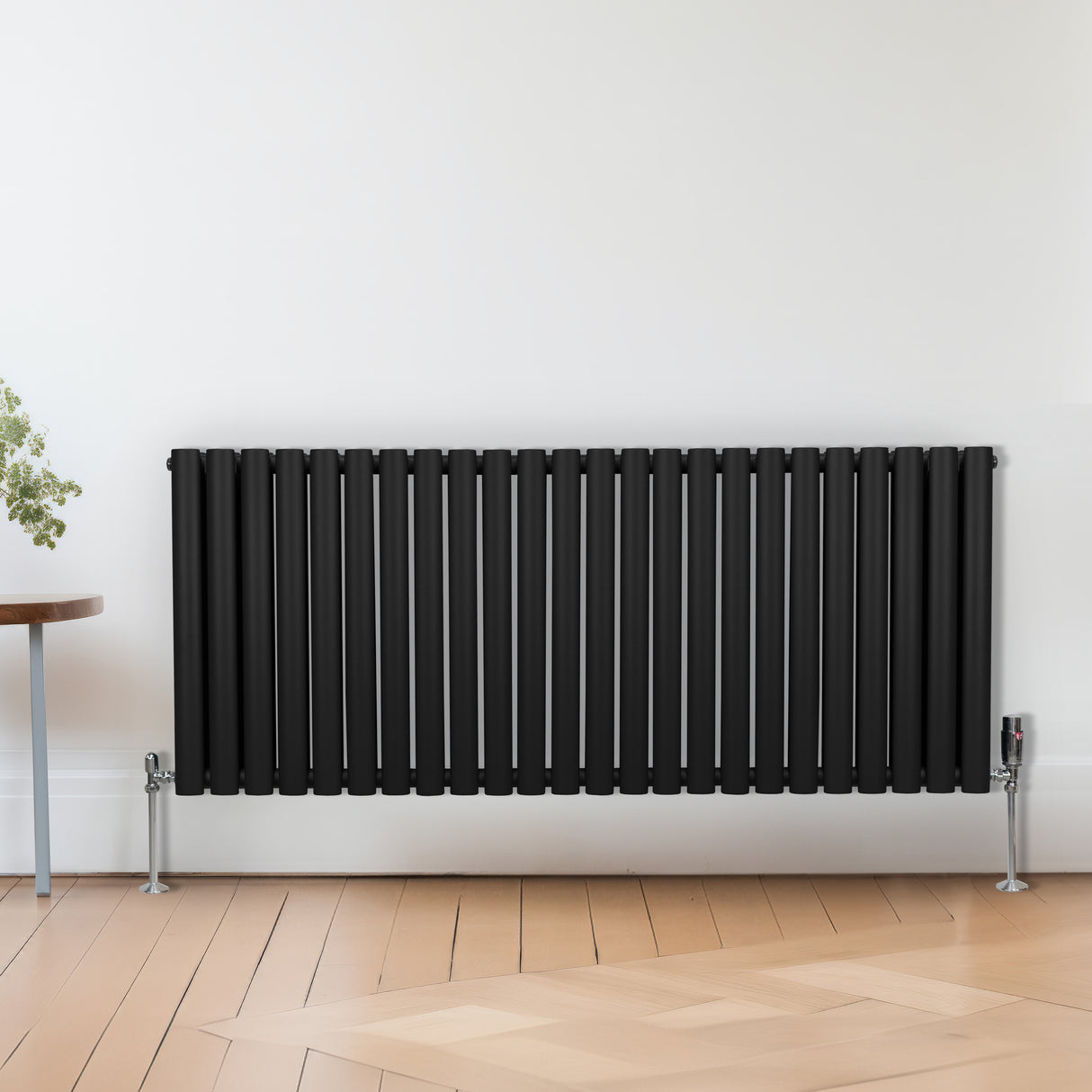 Svart radiator med förkromade termostatventiler, slanka och moderna linjer, placerad mot en ljus vägg och trägolv