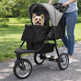 Grå husdjursvagn med en glad hund inuti, stora hjul och en mjuk, vadderad sittdel, perfekt för promenader i parken