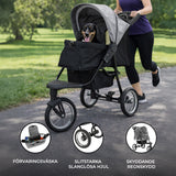 Grå husdjursvagn med en hund i selen, stora slanglösa hjul och ett skyddande regnskydd, perfekt för promenader i parken