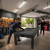 Grått 7-i-1 spelbord med dartpaket och LED-lampa, två personer spelar biljard i en garageinredning med verktyg och cyklar
