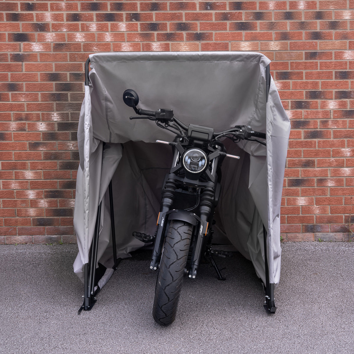 Motorcykel skyddad av en grå täckställning med en robust ram, placerad mot en tegelvägg för extra skydd och säkerhet