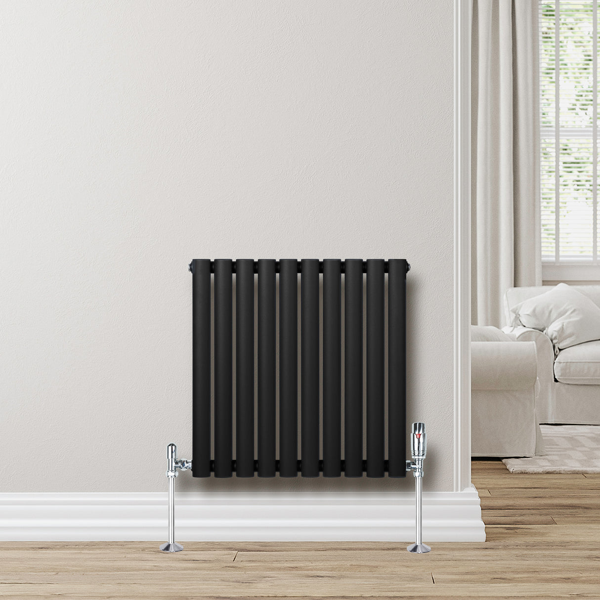 Oval svart radiator med sju vertikala rör, monterad på vägg, med kromade ventiler och träplankgolv i bakgrunden