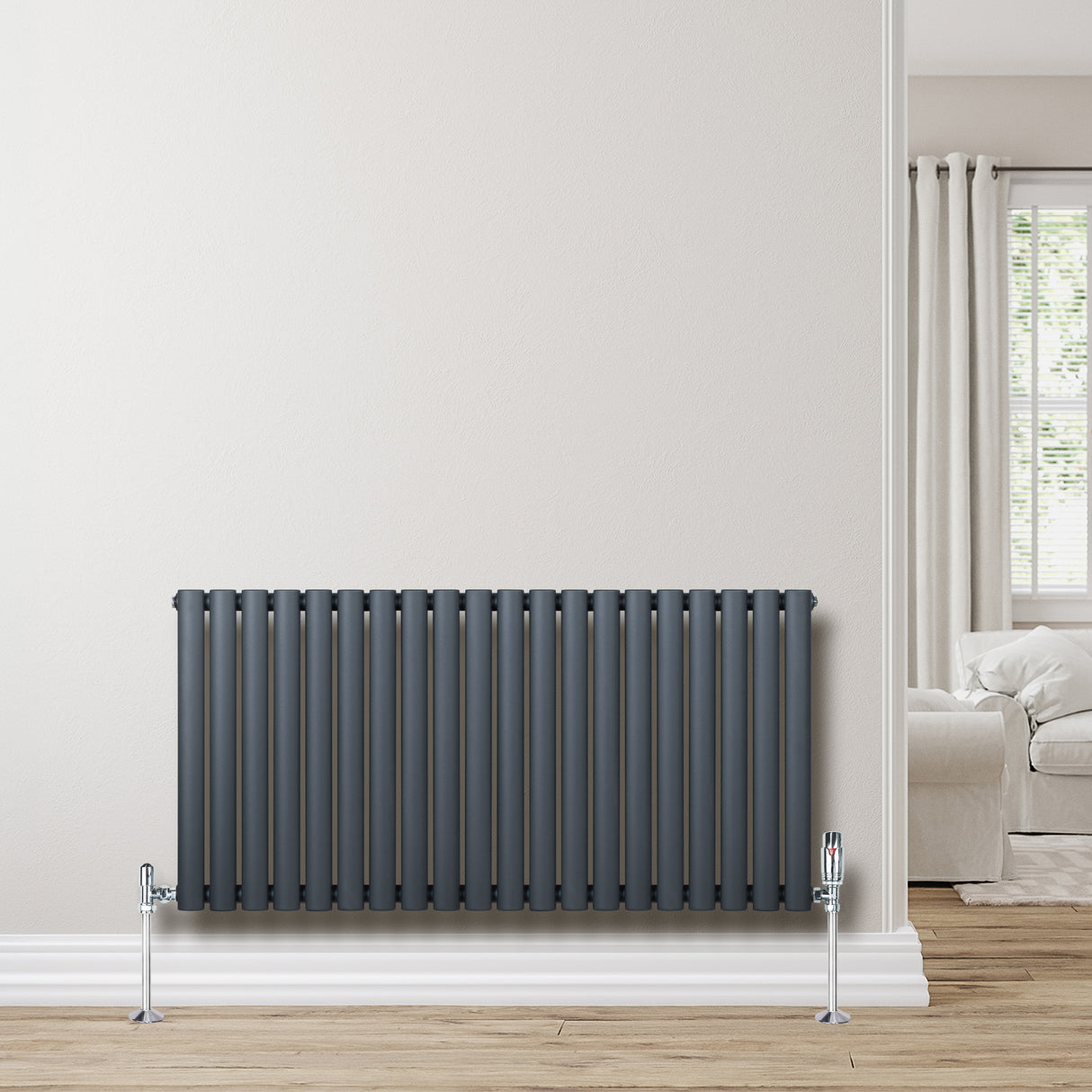Oval enkelkolonnsradiator i antracitgrå med släta, runda rör och kromade ventiler, placerad mot en ljus vägg i ett modernt rum