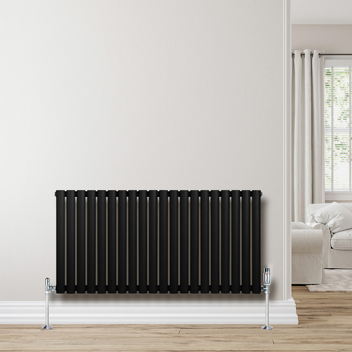 Svart oval enkelkolonnsradiator med släta, vertikala ribbor, monterad på vägg, kompletterad med kromade ventiler och trägolv