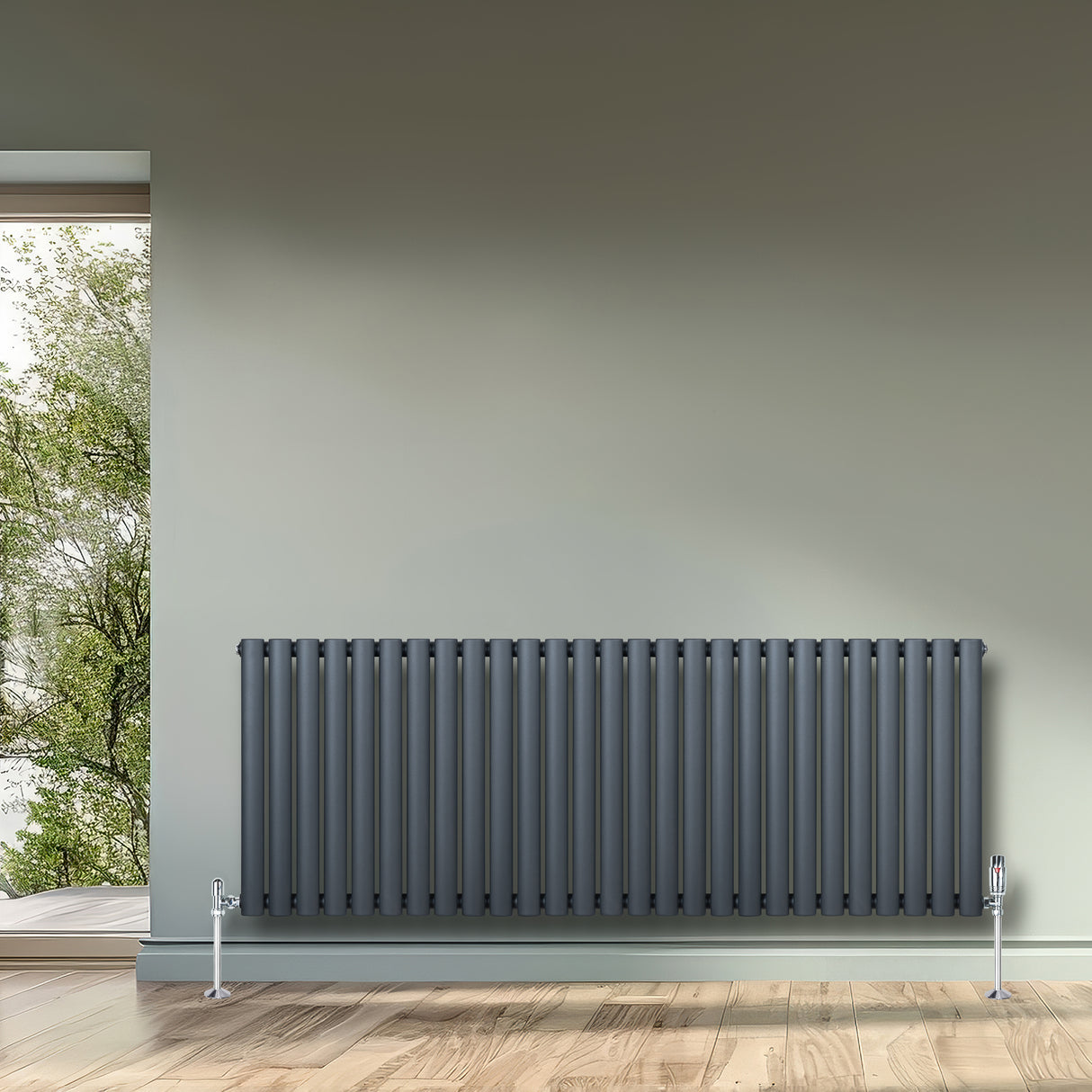Oval antracitgrå enkelkolonnsradiator med vertikala ribbor, placerad mot en ljus vägg och trägolv, ger modern värme och stil