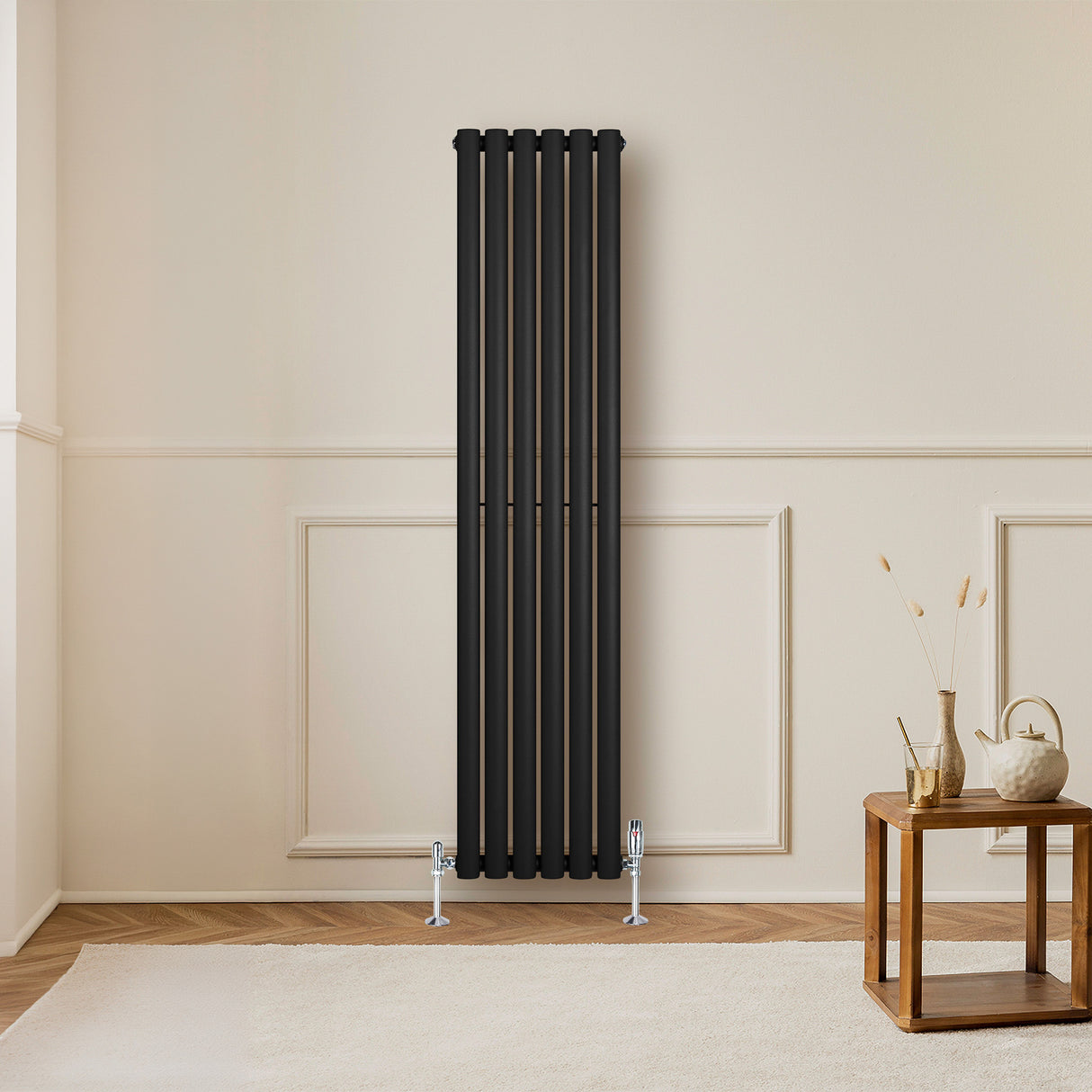 Oval svart enkelkolonnsradiator med ventiler, 1600 mm x 360 mm, placerad i ett ljust rum med trädetaljer och en soffbord
