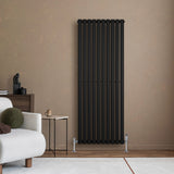 Svart oval enkelkolonnsradiator med släta ytor och vertikala ribbor, placerad mot en beige vägg i ett modernt rum