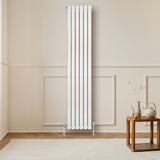 Oval vit enkelkolonnsradiator med släta, vertikala ribbor, placerad på en ljus vägg i ett stilrent rum med trädetaljer