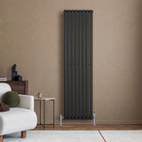 Svart oval enkelkolonnsradiator med slanka linjer, placerad mot en beige vägg, kompletterad med ventiler och stilren inredning