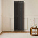 Oval svart enkelkolonnsradiator med ventiler, 1800 mm x 600 mm, placerad på en ljus vägg i ett modernt rum med trädetaljer