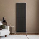 Oval svart enkelkolonnsradiator med släta, vertikala ribbor, placerad mot en beige vägg i en modern inredning