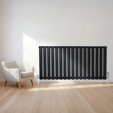 Svart platt enkelkolumnsradiator med ventiler, 600 mm x 1190 mm, placerad på en ljus trägolv i ett modernt rum med en stol