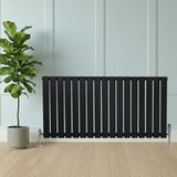 Svart platt enkelkolumnsradiator med ventiler, 600 mm x 1190 mm, placerad framför en grön växt på golv av trä