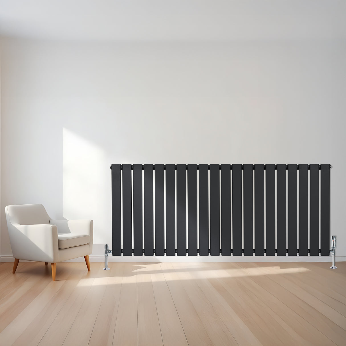 Platt enkelkolumnsradiator i antracitgrå med vertikala lameller, placerad mot en ljus vägg, med en vit fåtölj i närheten