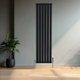 Svart platt enkelkolumnsradiator med ventiler, 1600 mm x 420 mm, placerad mot en ljus vägg med en grön växt i kruka i förgrunden