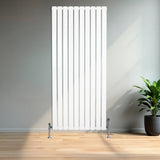 Vit platt enkelkolumnsradiator med ventiler, 1600 mm x 700 mm, stående mot en vägg i ett rum med trägolv och grön växt