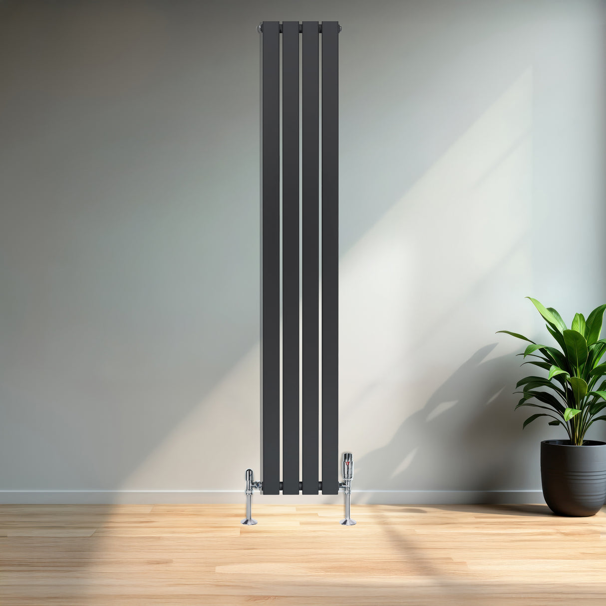 Platt enkelkolumnsradiator i antracitgrå med fyra vertikala paneler, stående på golvet i ett ljust rum med växt i kruka