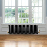 Svart traditionell 4-kolonnsradiator i metall med ventiler, placerad under ett stort fönster i ett ljust rum med trägolv