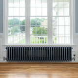 Traditionell antracitgrå 4-kolonnsradiator med släta ytor, placerad under ett stort fönster med trädetaljer och parkettgolv