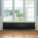 Svart traditionell 4-kolonnsradiator i metall med glänsande yta, placerad under ett stort fönster med trädetaljer och parkettgolv