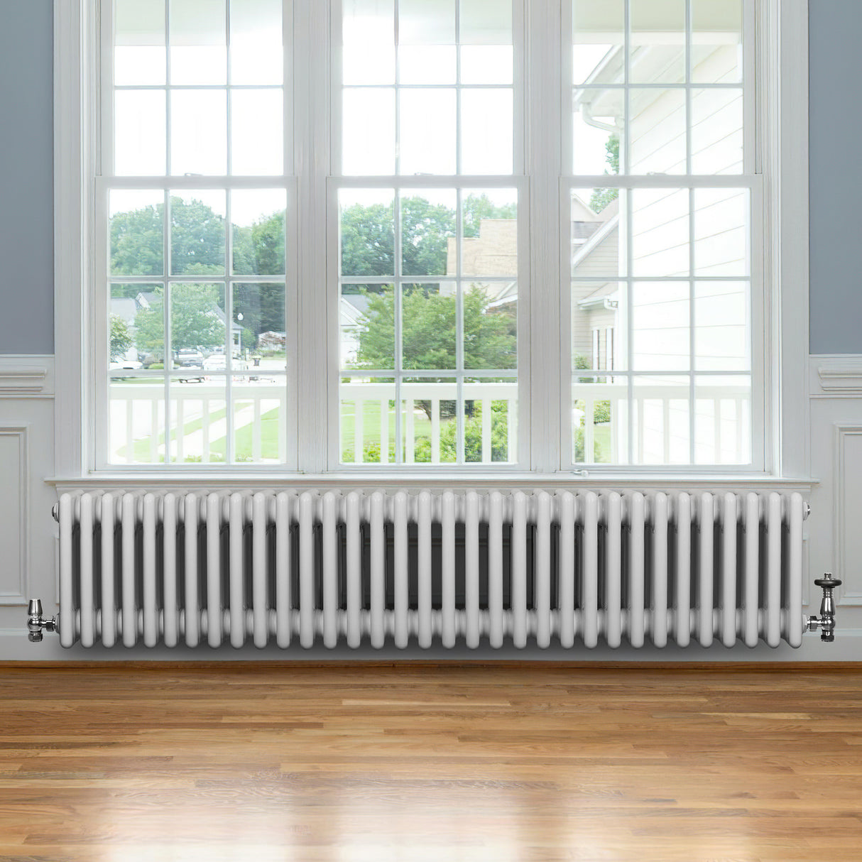 Traditionell vit 4-kolonnsradiator i metall, 300 x 1505 mm, placerad under ett stort fönster med trädetaljer och parkettgolv